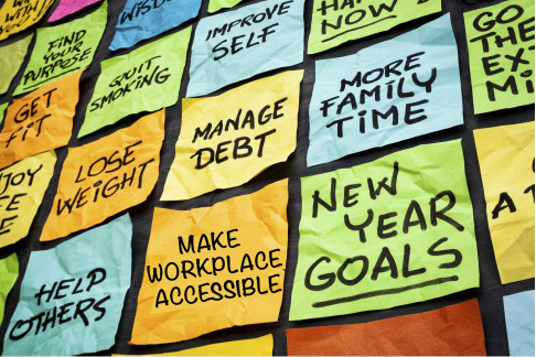 Man colored square post-it notes on a dark surface. Each post-it note bears a New Year's resolution, including one that says "make workplace accessible".